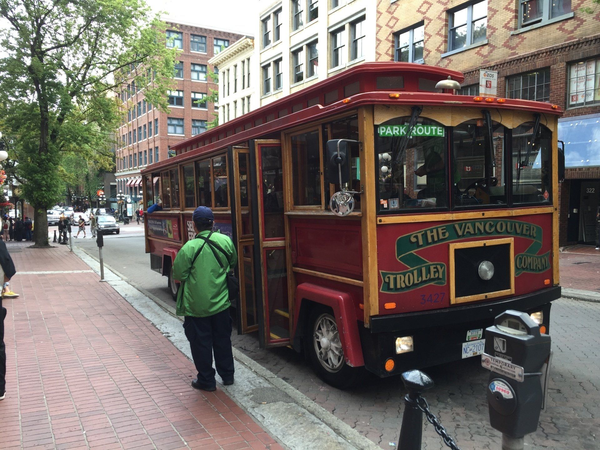 Red trolley in Vancouver with passengers, parked on a brick sidewalk on a city street.