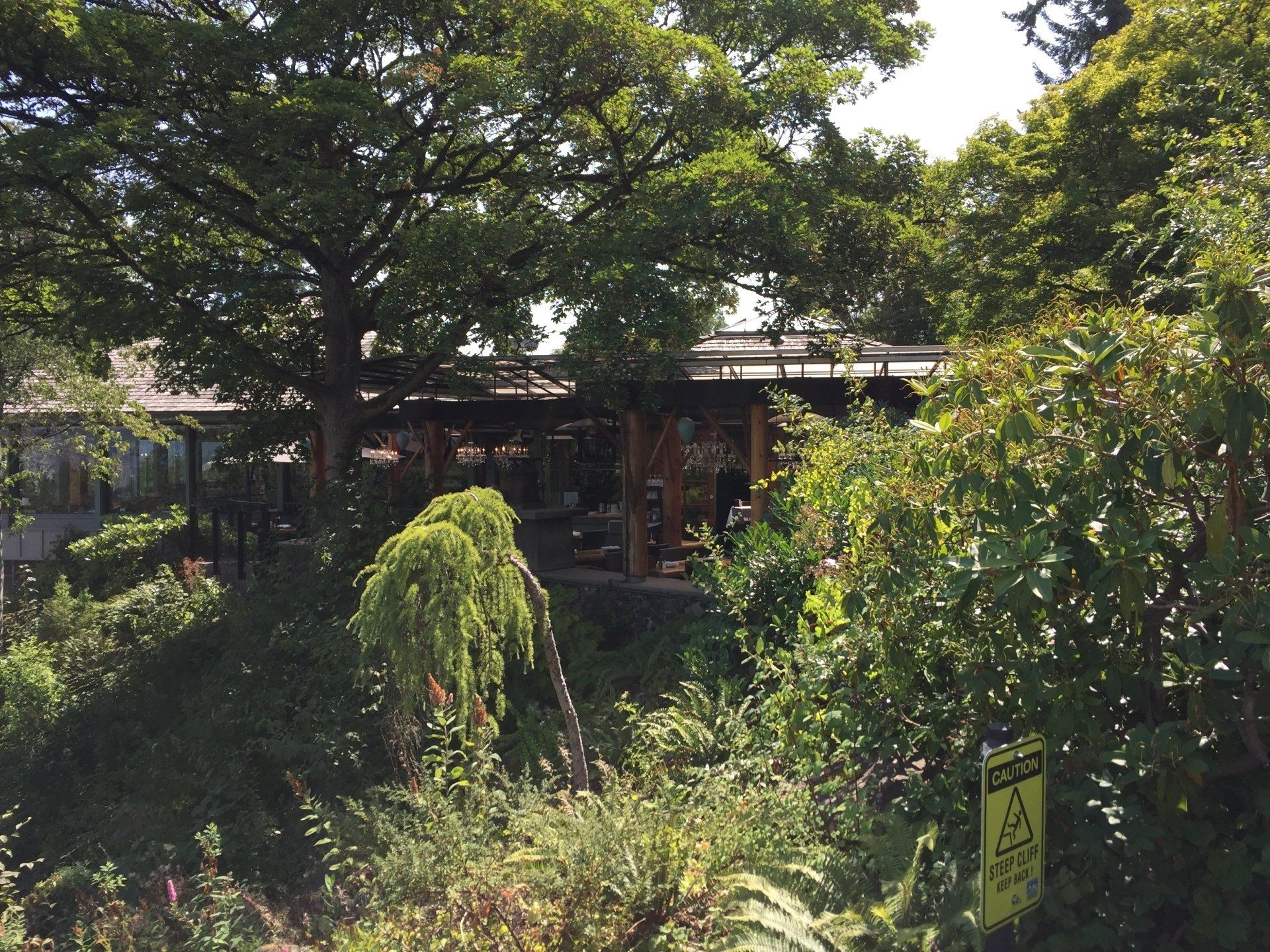 Lush greenery surrounds a wooden building, partially obscured. A yellow sign with caution symbols is visible.