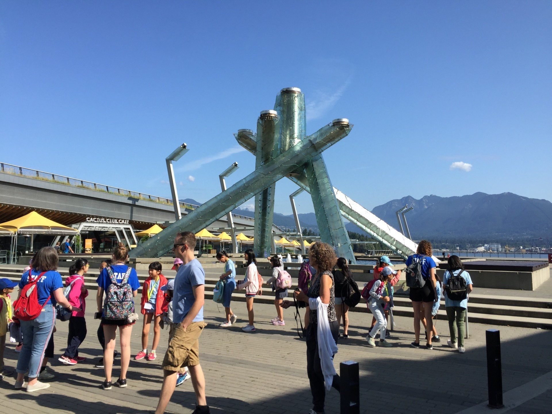 People at Olympic Cauldron in Vancouver, BC, under blue sky. Mountains in the background.