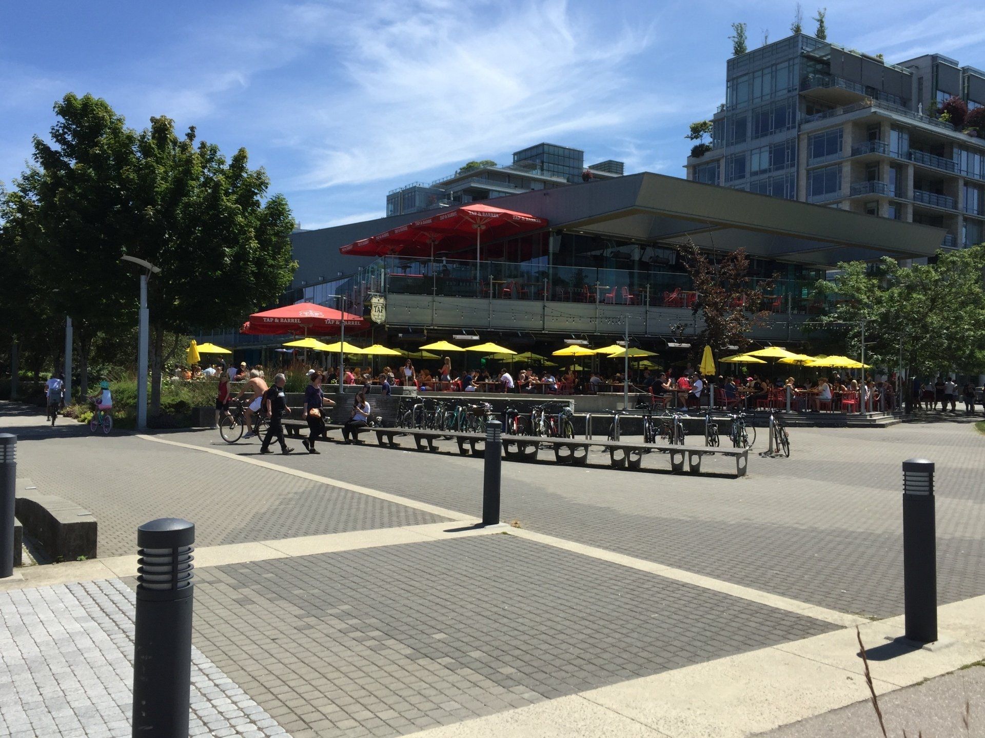 Outdoor restaurant with red and yellow umbrellas. People seated at tables, building in background.