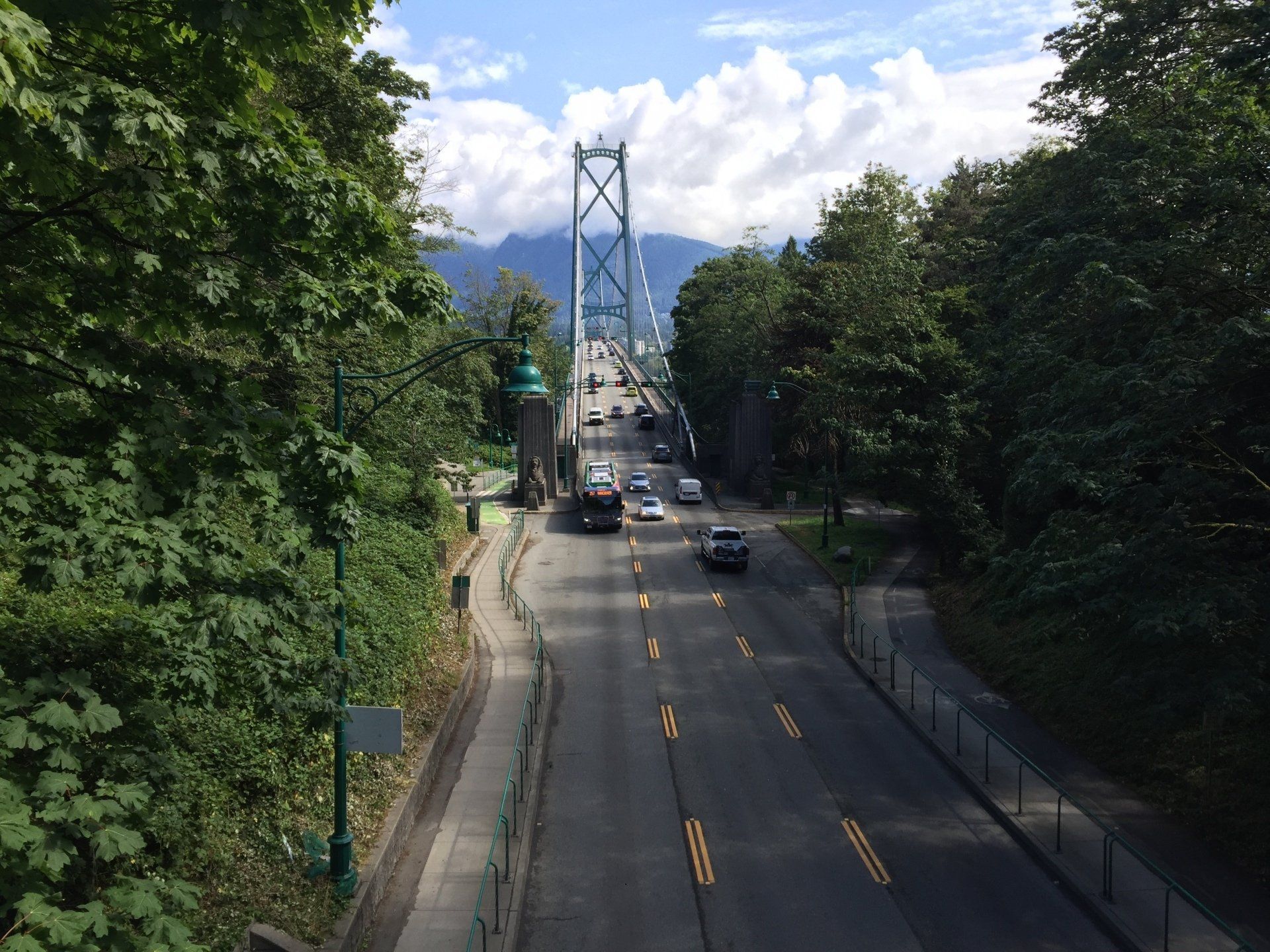 Road leading to the Lions Gate Bridge in Vancouver, BC, with cars and lush greenery.