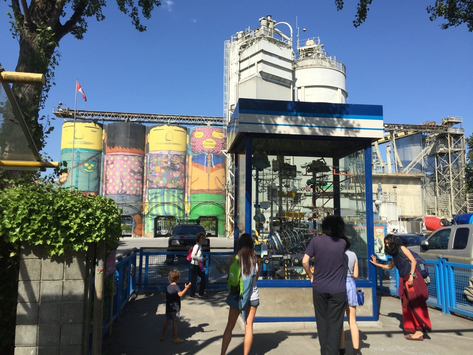 Colorful silos with painted murals, people near a blue structure on a sunny day.