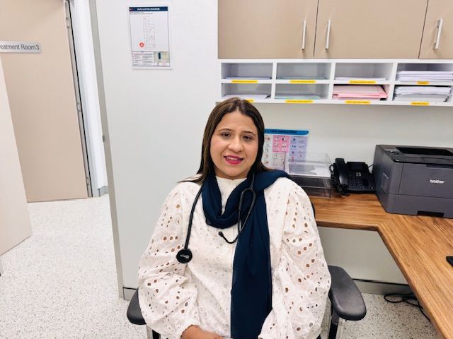 A woman is sitting at a desk with a stethoscope around her neck.