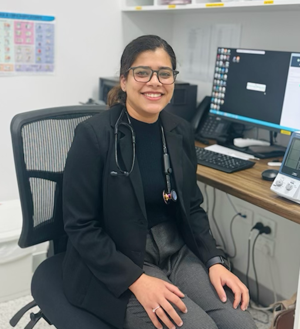 A woman is sitting at a desk with a stethoscope around her neck.