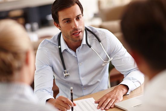 A doctor is sitting at a table talking to two patients.