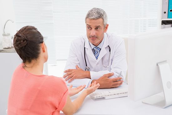 A doctor is talking to a patient who is sitting at a desk.