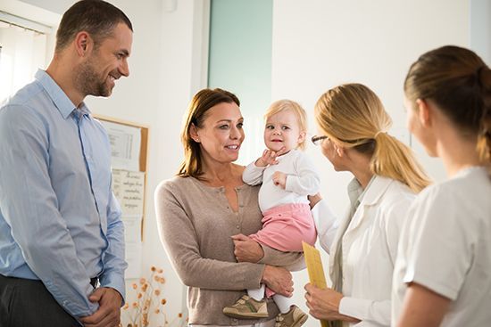 A woman is holding a baby while talking to a doctor.