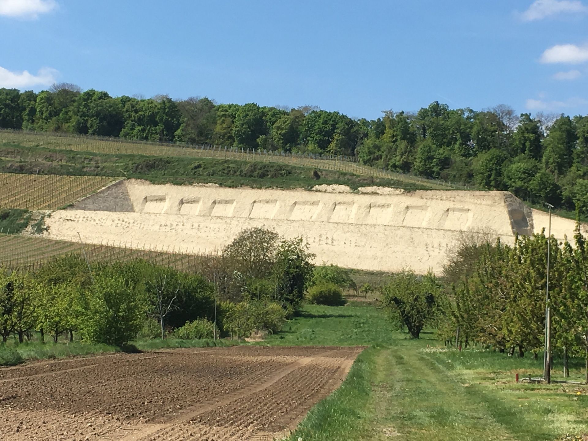 Weißliches, rechteckiges Gebäude, das in einen Hang gebaut ist und mehrere gleichmäßig verteilte Öffnungen aufweist, 