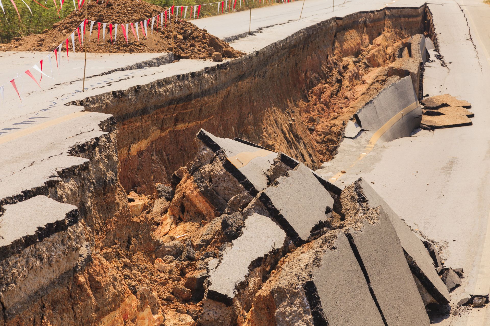 Die Straße ist stark beschädigt; ein großer Riss weist freiliegende Erde, Schutt und aufgerissenen Asphalt auf.