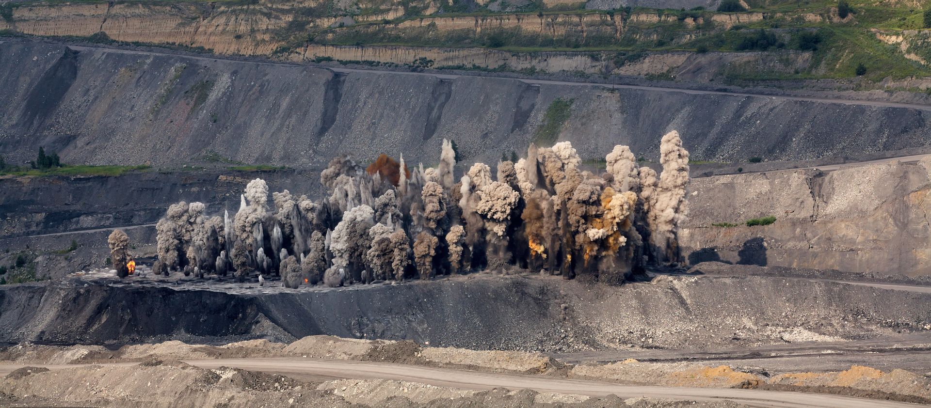 Sprengung in einem Steinbruch, eine Gesteins- und Staubwolke wird durch eine Explosion aufgewirbelt.