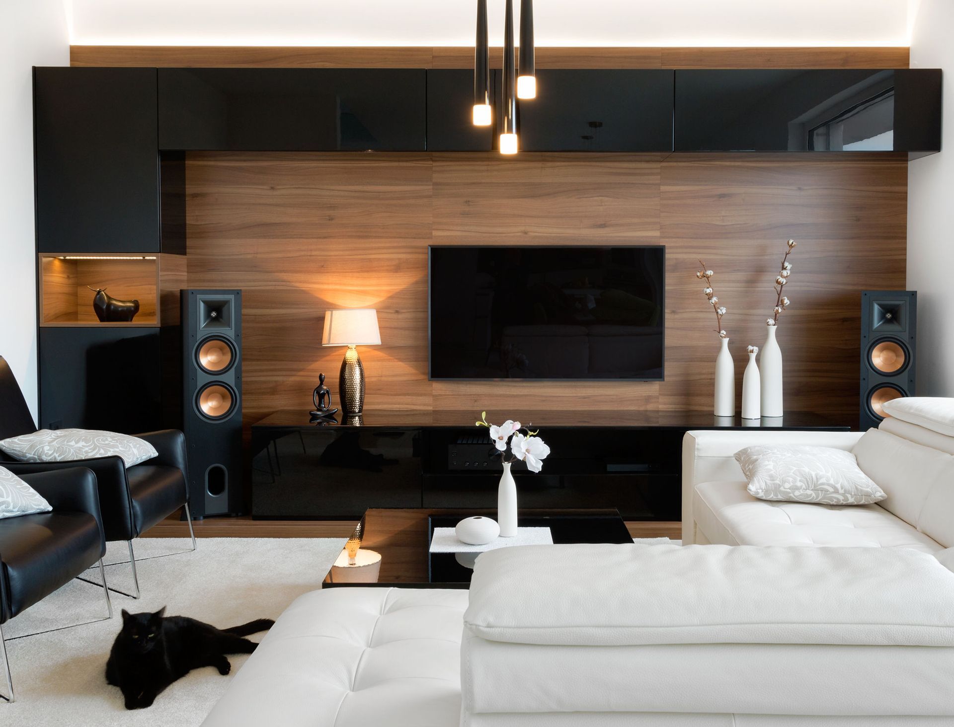 Modern black-and-white living room with a wall-mounted TV, speakers, white sectional sofa, and warm lighting