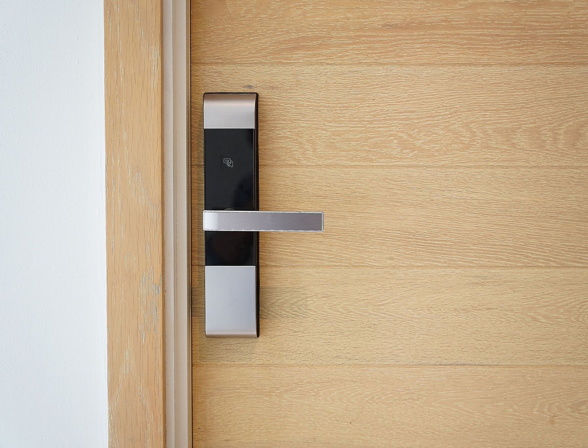 Modern silver door handle on a light wooden door near a white wall