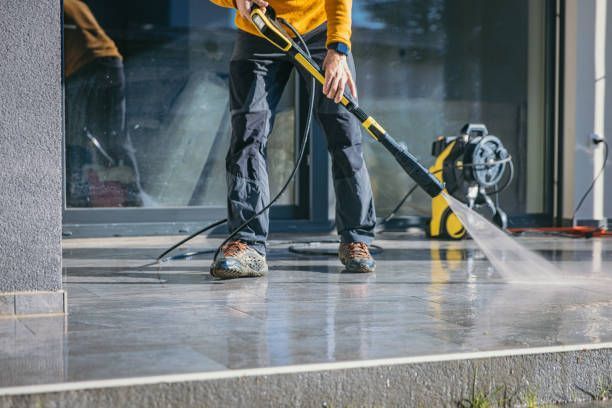 Person power washing a concrete patio with a yellow and black pressure washer.