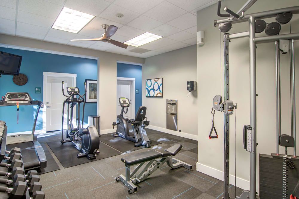 Gym with exercise equipment like treadmill, weights, elliptical, and cable machine.