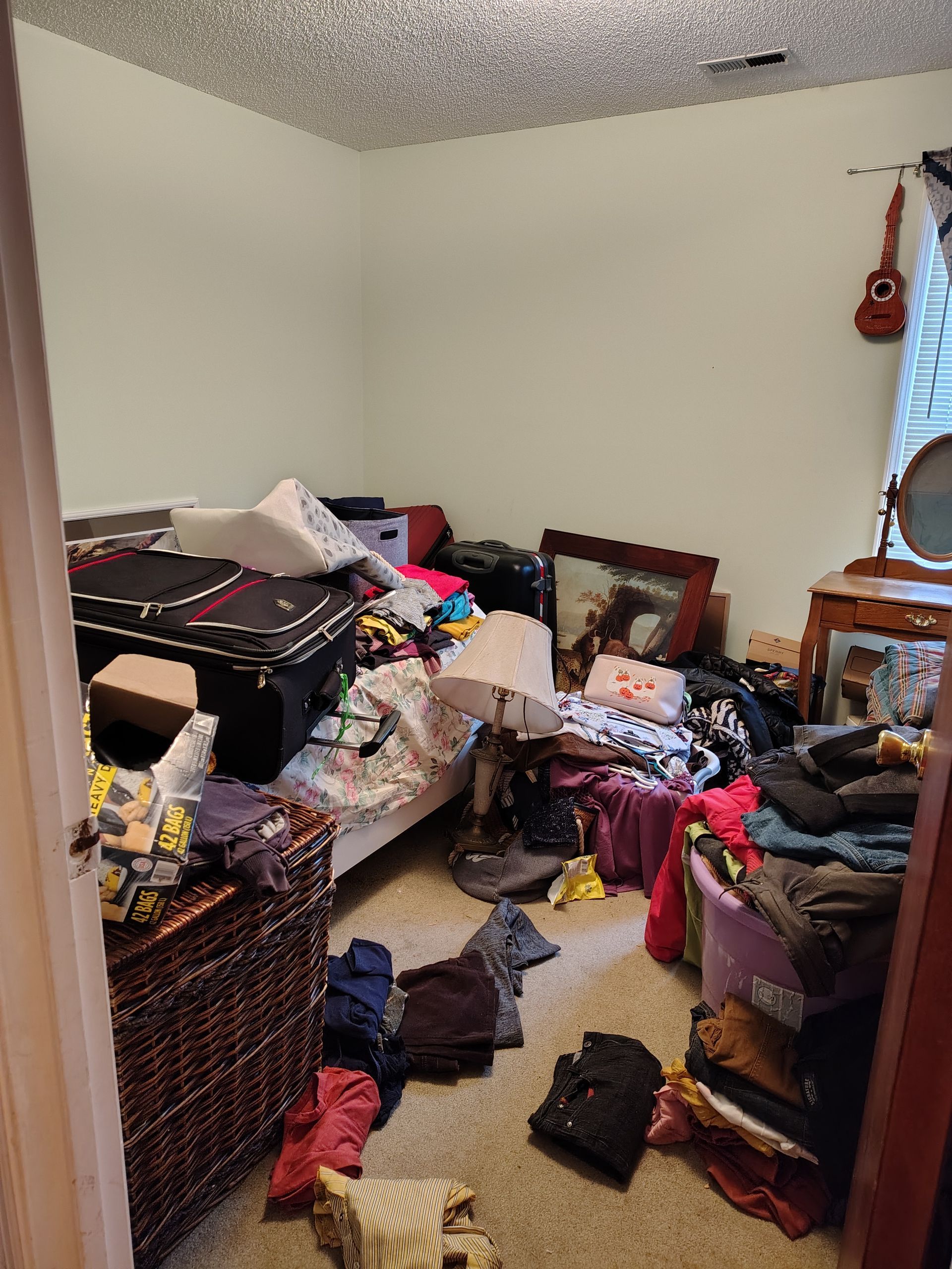 A bedroom with a lot of clothes on the floor and a bed.