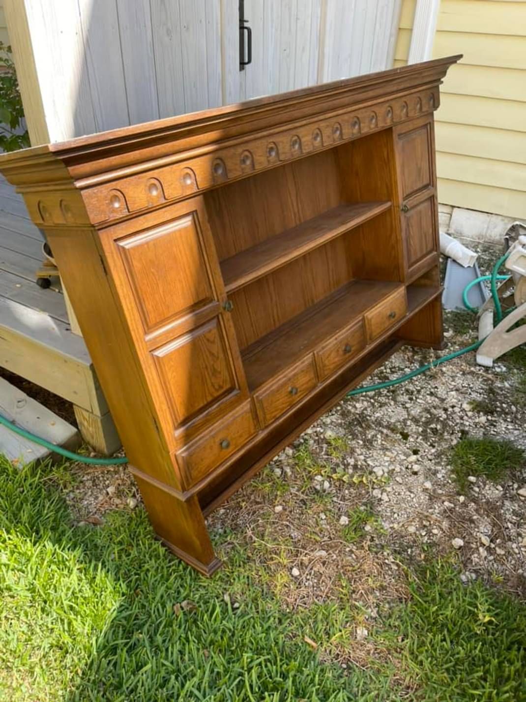 A wooden hutch is sitting in the grass in front of a house.