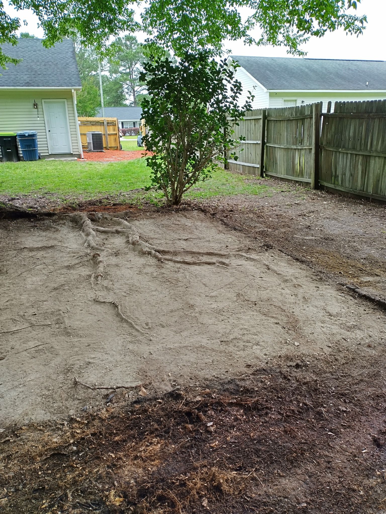 A dirt yard with a wooden fence and a house in the background.