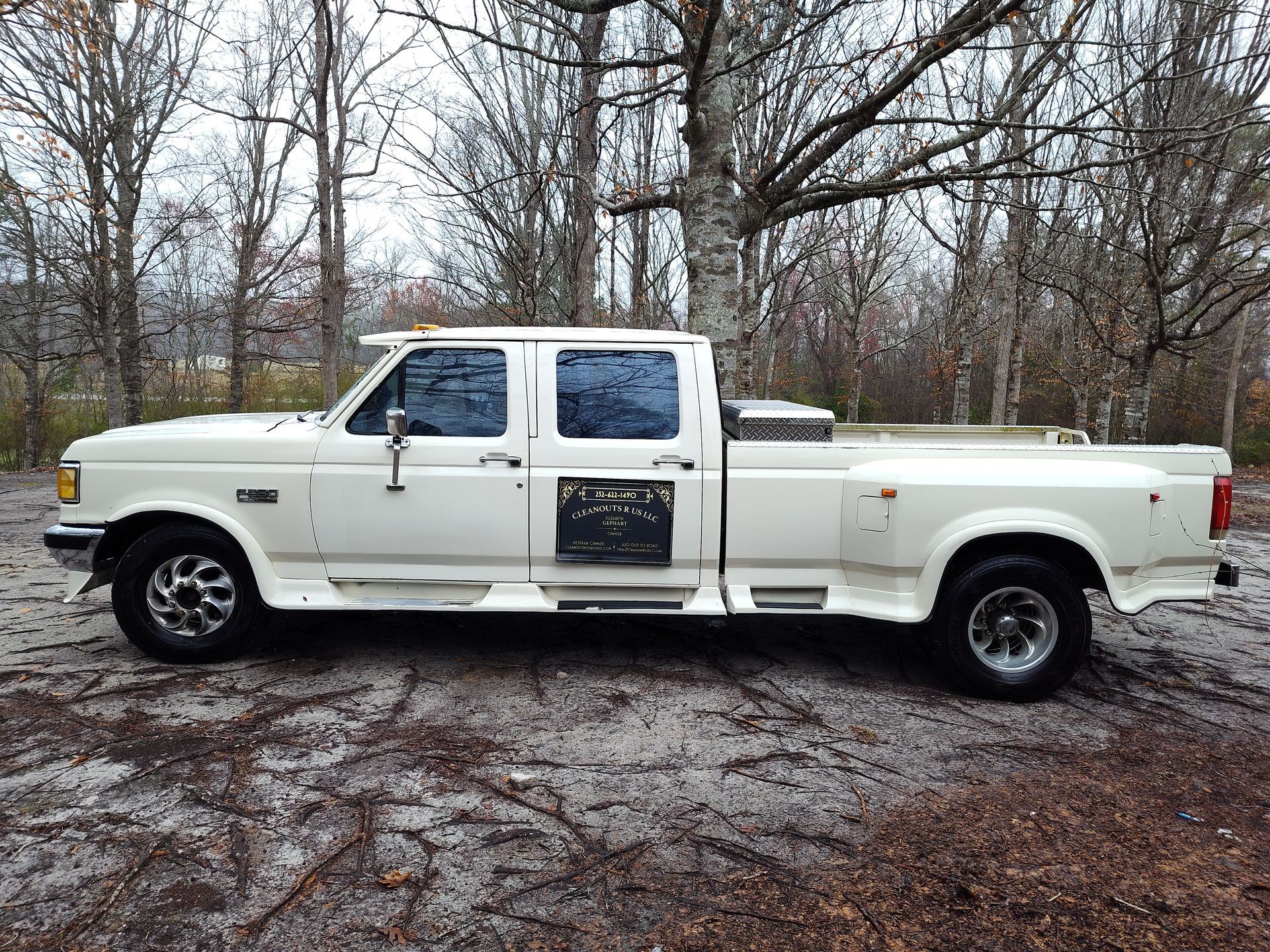 A white pickup truck is parked in front of a forest.