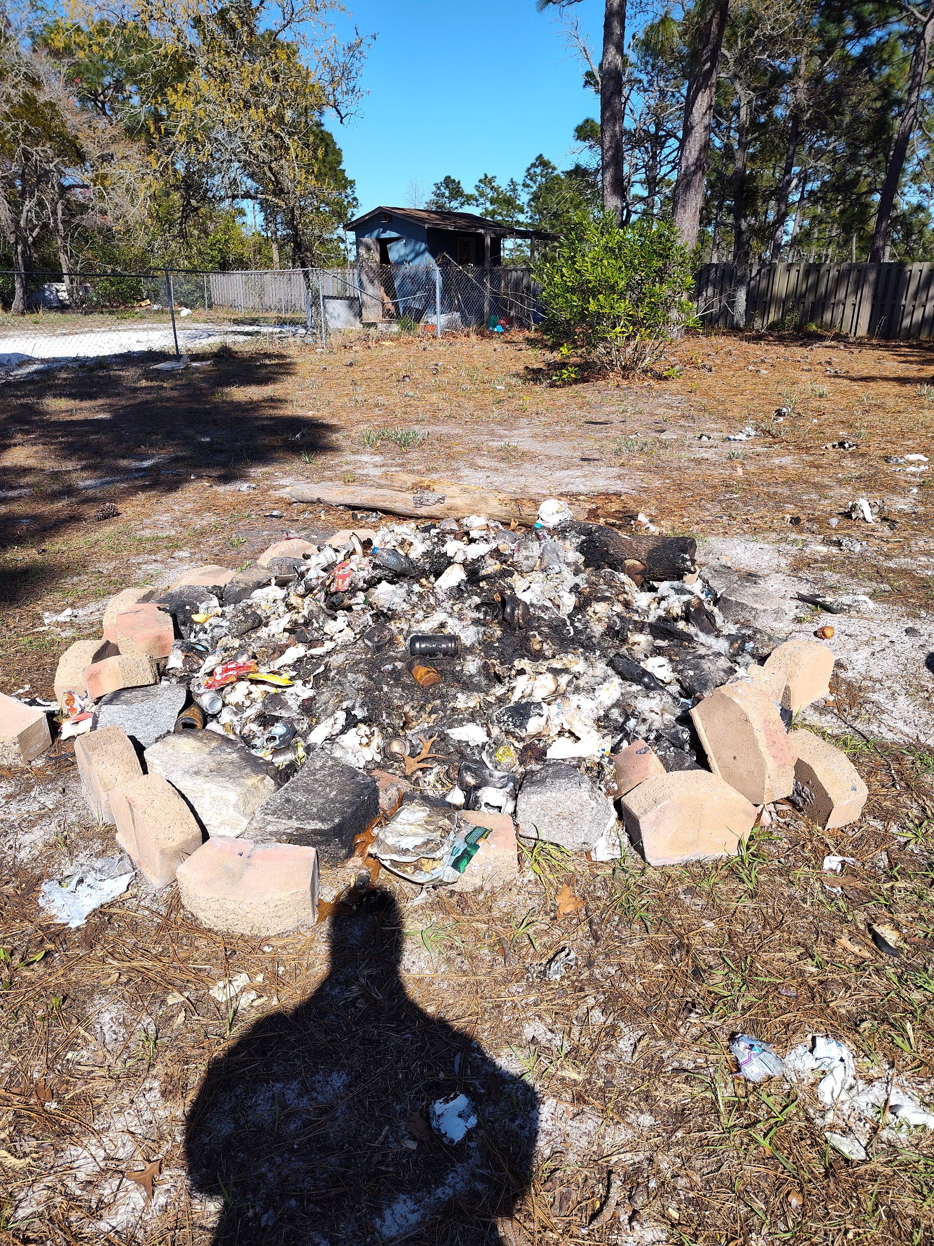 A shadow of a person is cast on the ground in front of a fire pit.