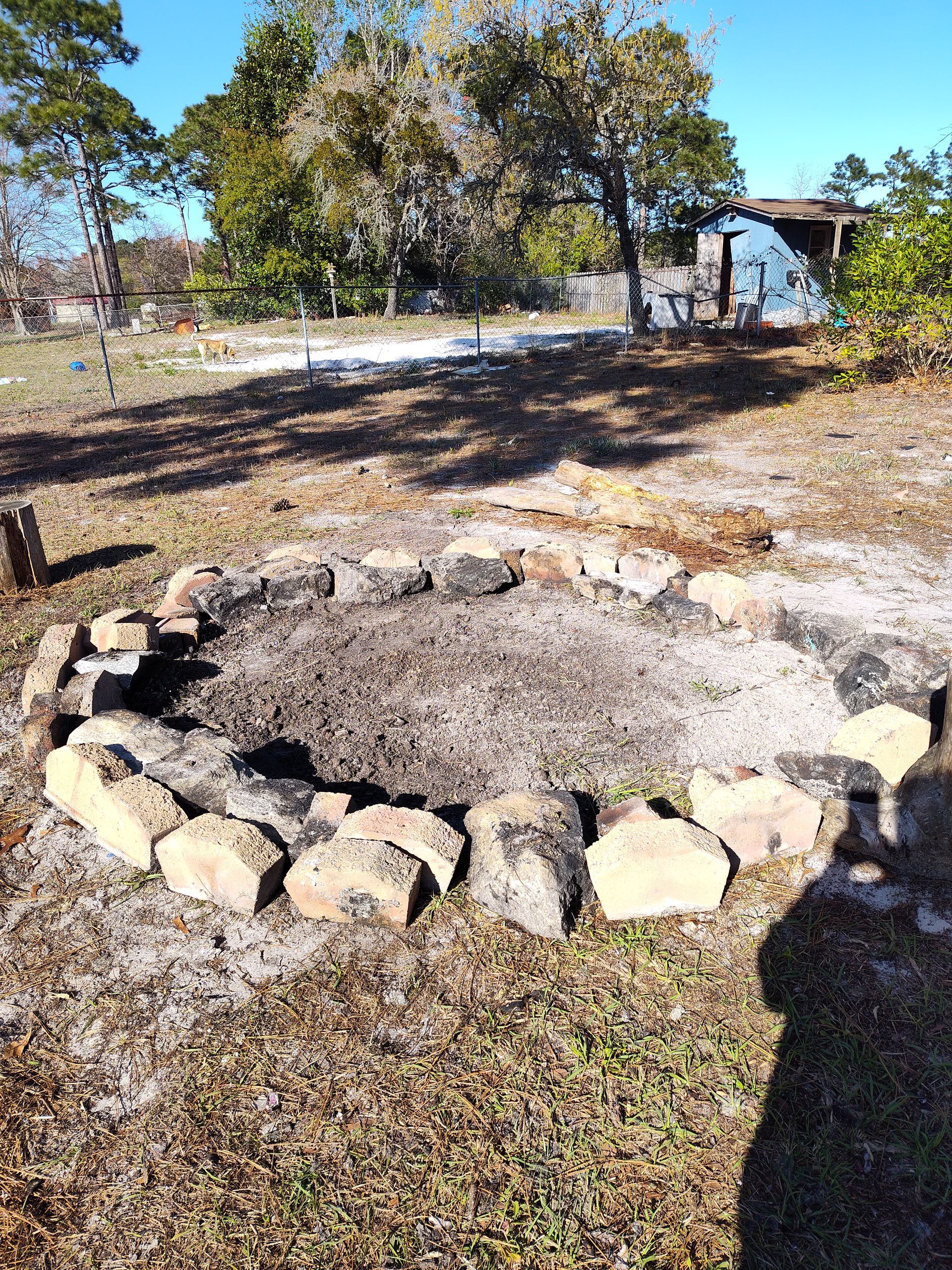 A fire pit in the middle of a grassy field with trees in the background.