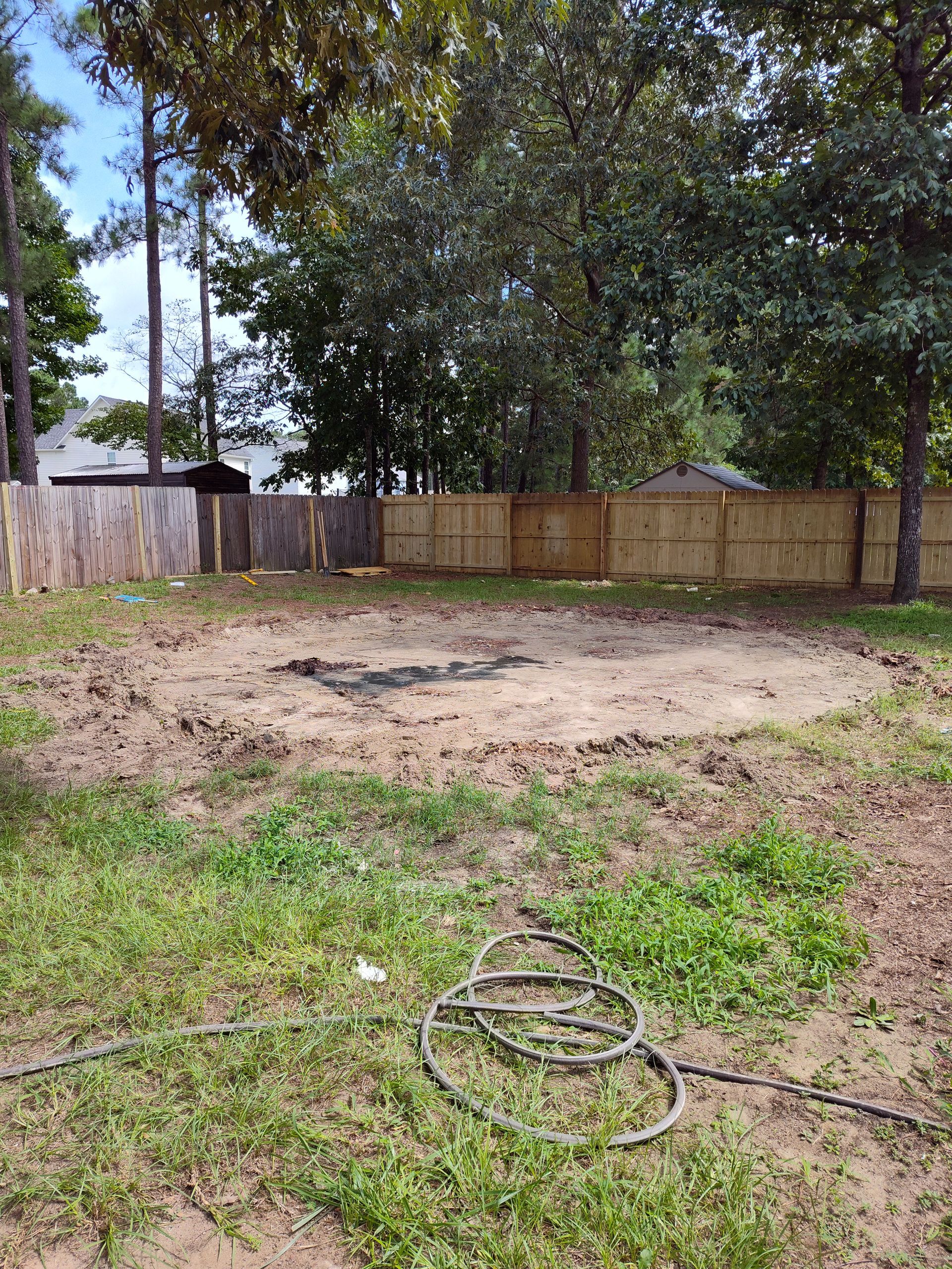 There is a hose in the middle of the grass in the backyard.