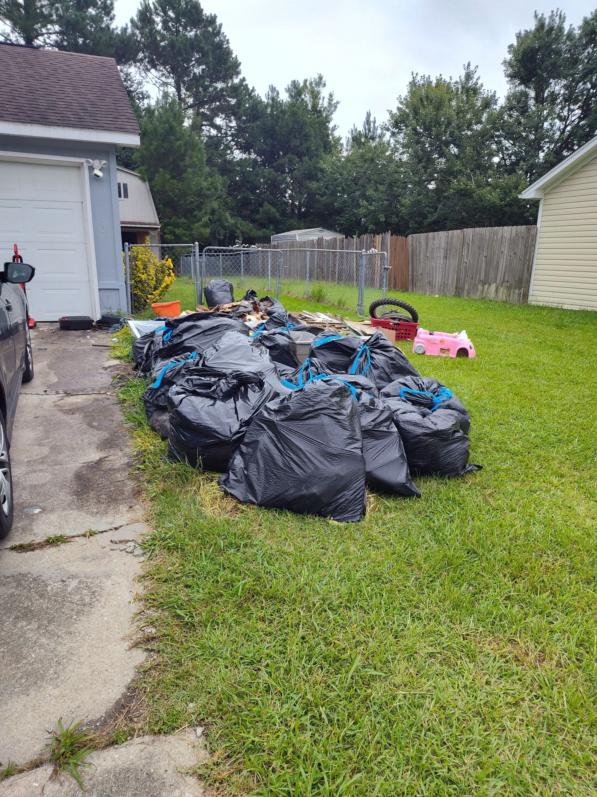 A pile of trash bags is sitting in the grass in front of a house.