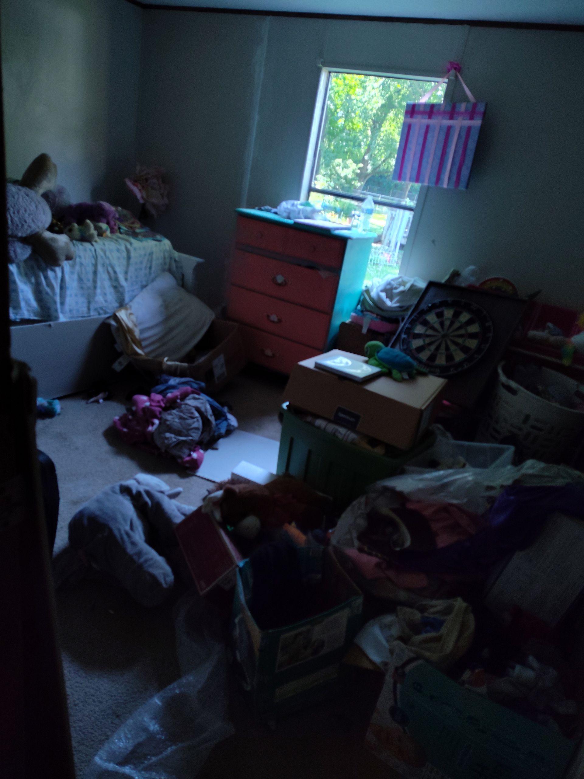 A messy room with a dart board and a dresser