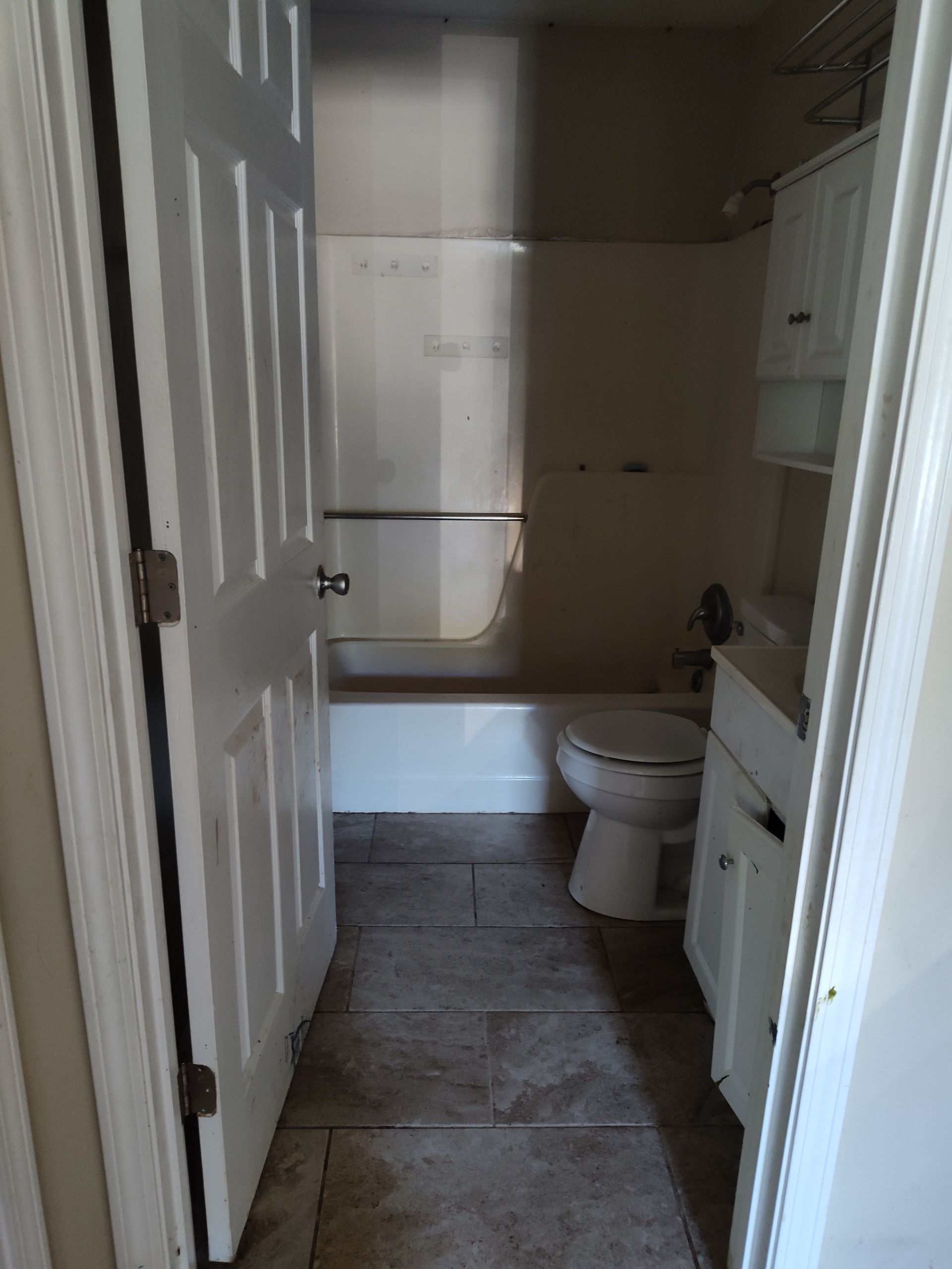 A bathroom with a toilet , bathtub , and cabinets.