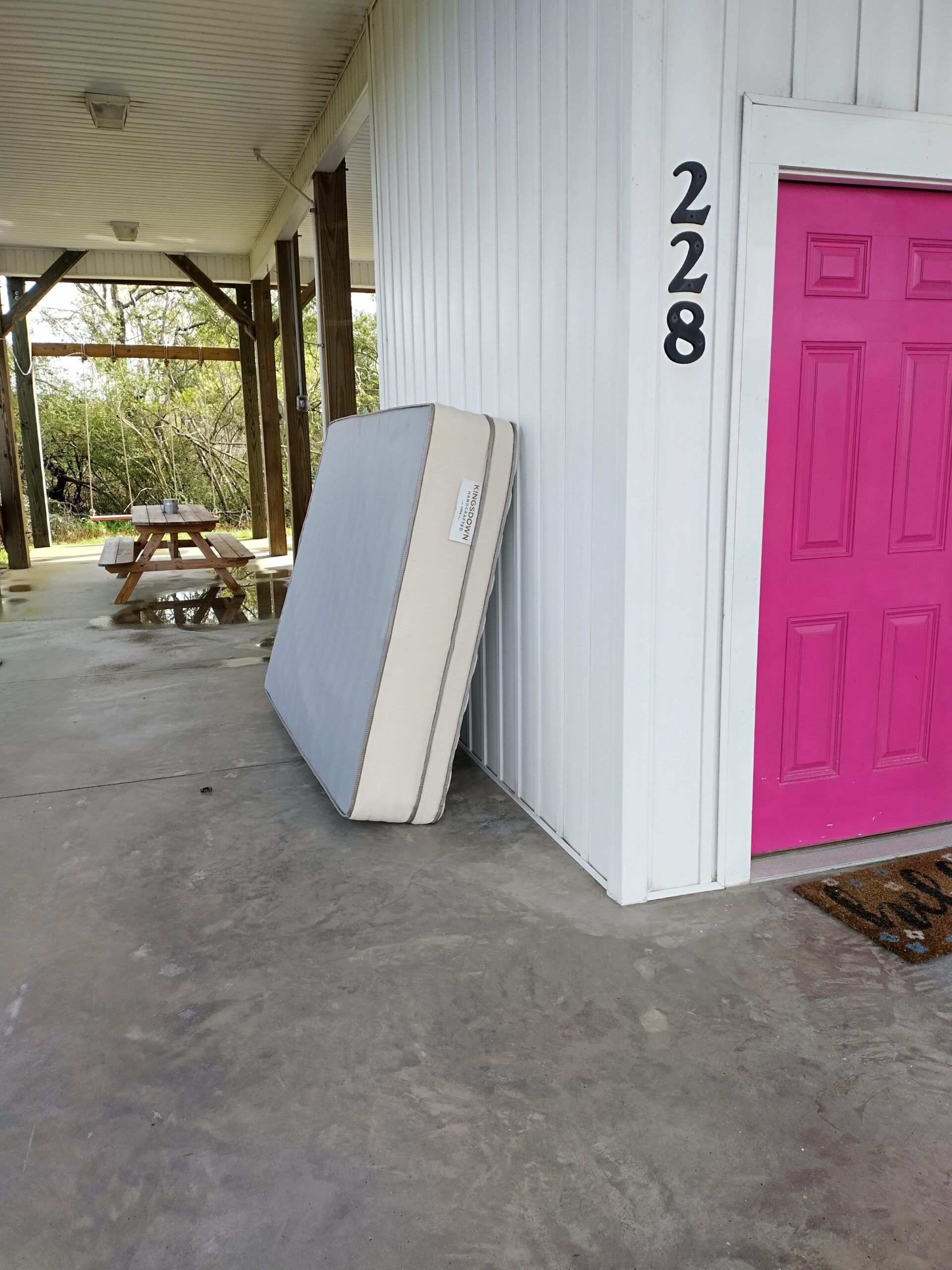 A mattress is sitting on the side of a building next to a pink door.
