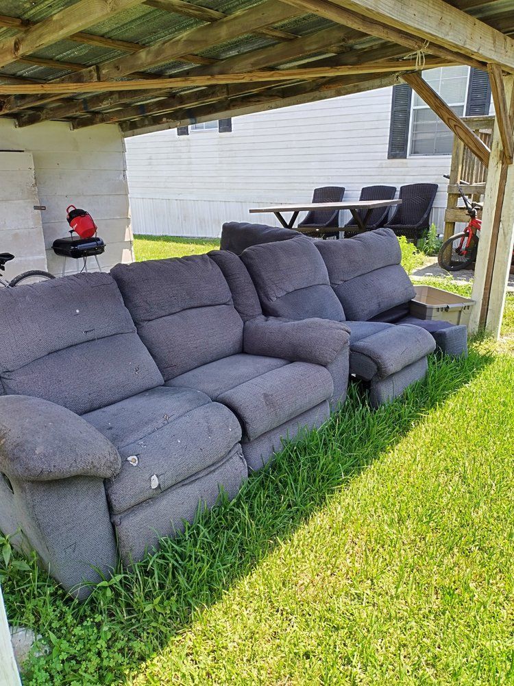 A couch is sitting in the grass under a covered area.
