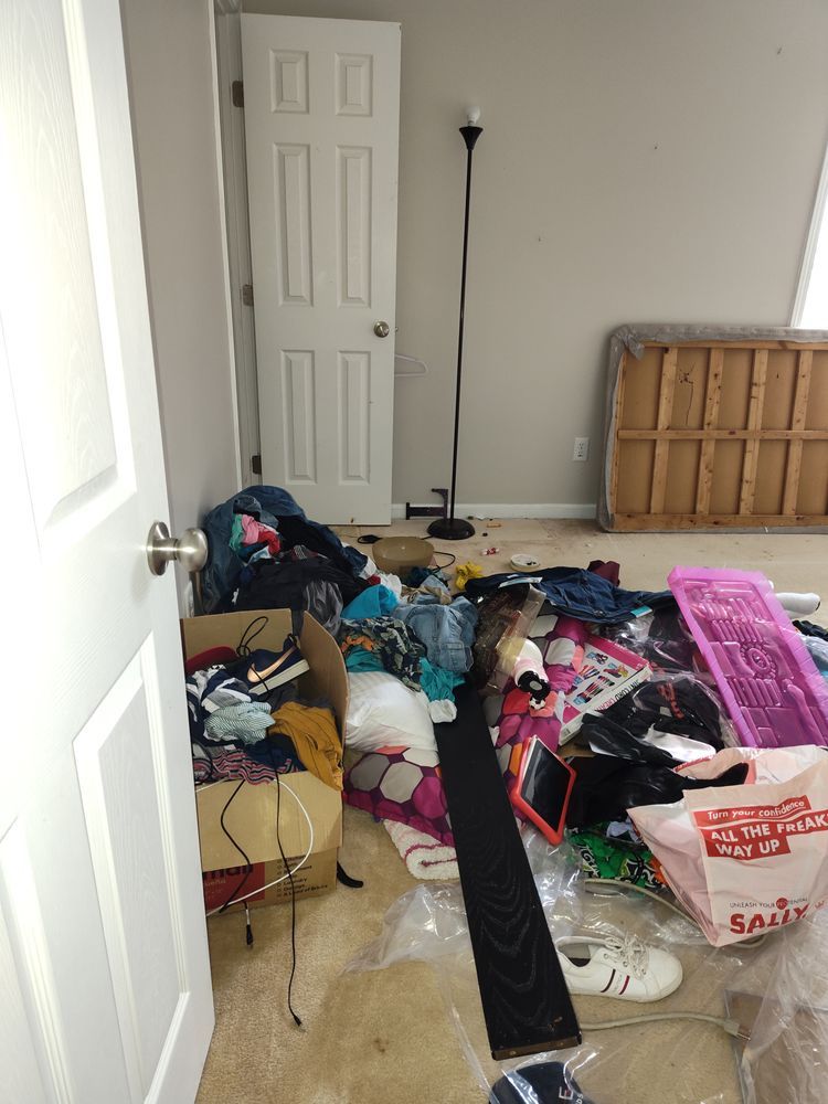 A messy room with a lot of clothes and boxes on the floor.