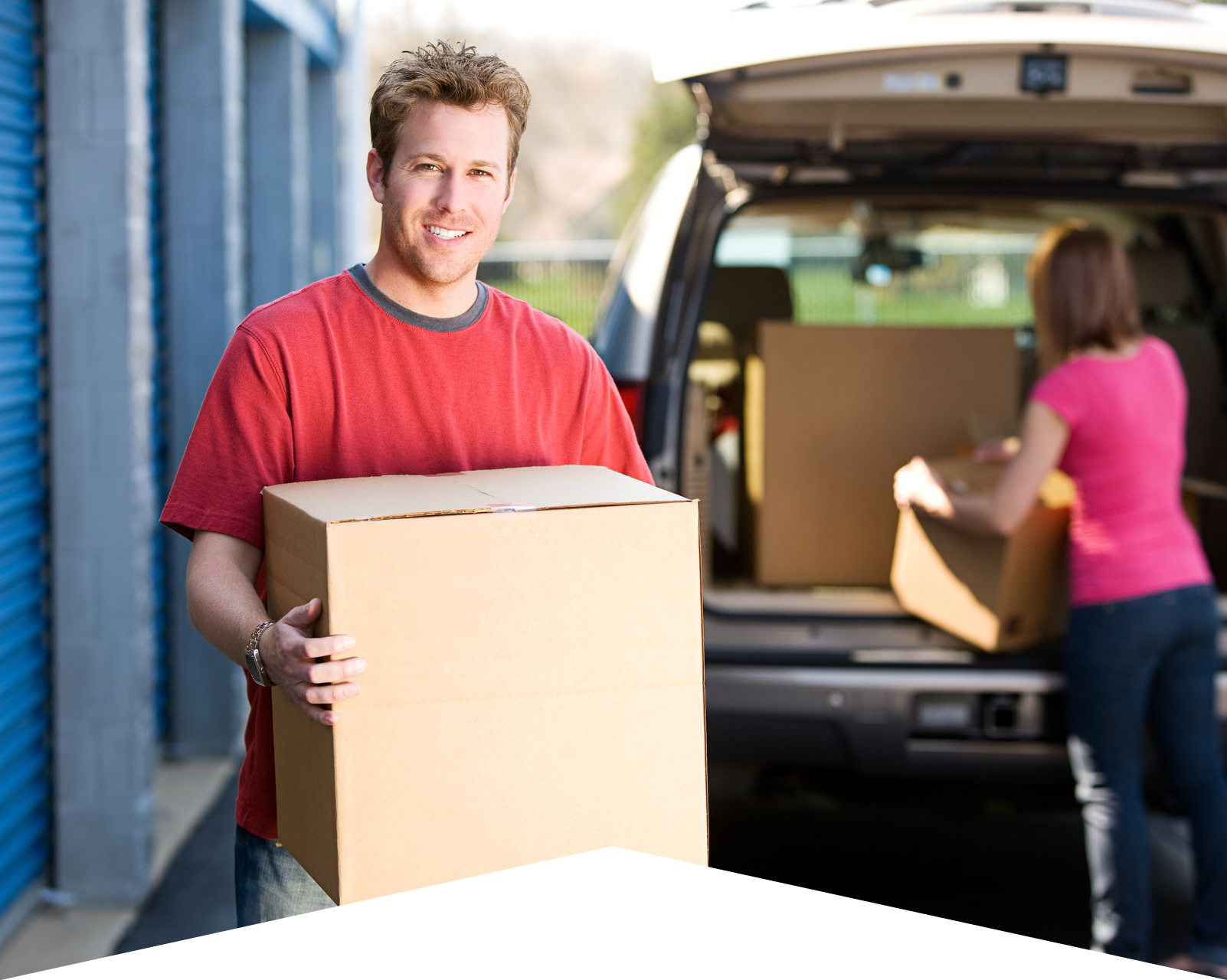 Man holding box outside of storage unit with woman unloading boxes from car