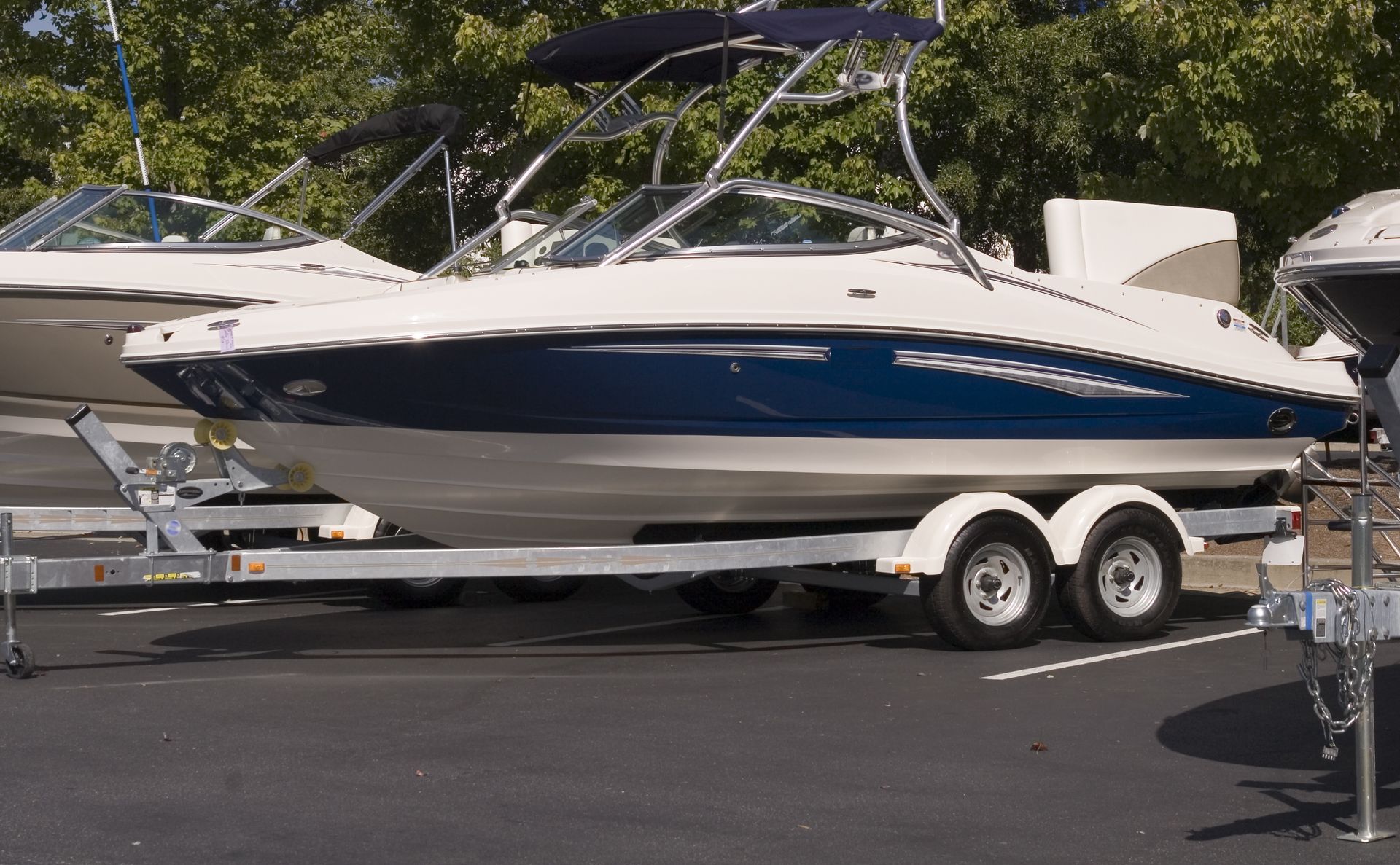 A blue and white boat is on a trailer in a parking lot.