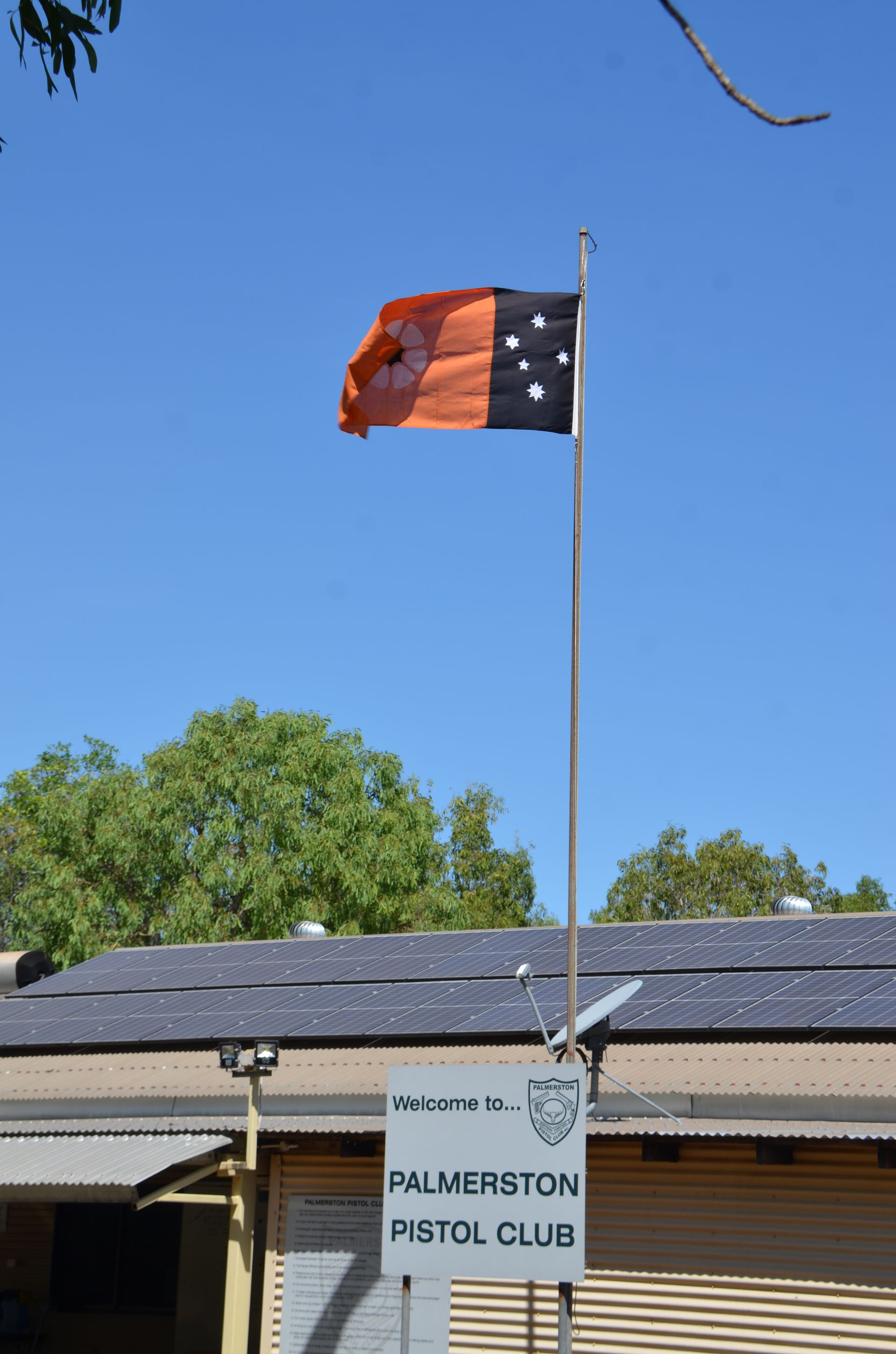 Flag of Palmerston Pistol Club, Northern Territory, Australia; orange and black design with white stars, flying in the wind.