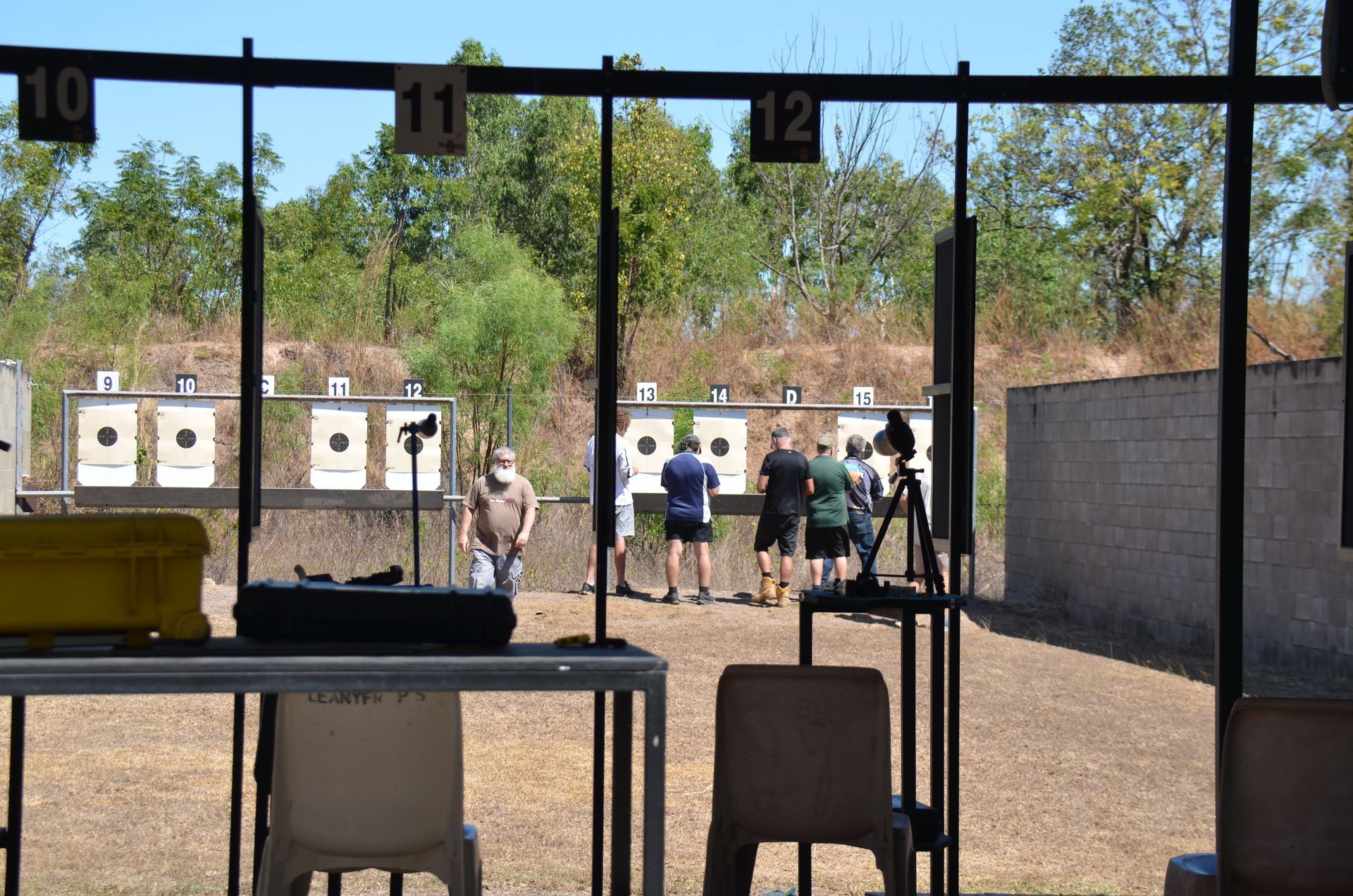People shooting at targets on a range; numbered stations, a table with gear in the foreground.