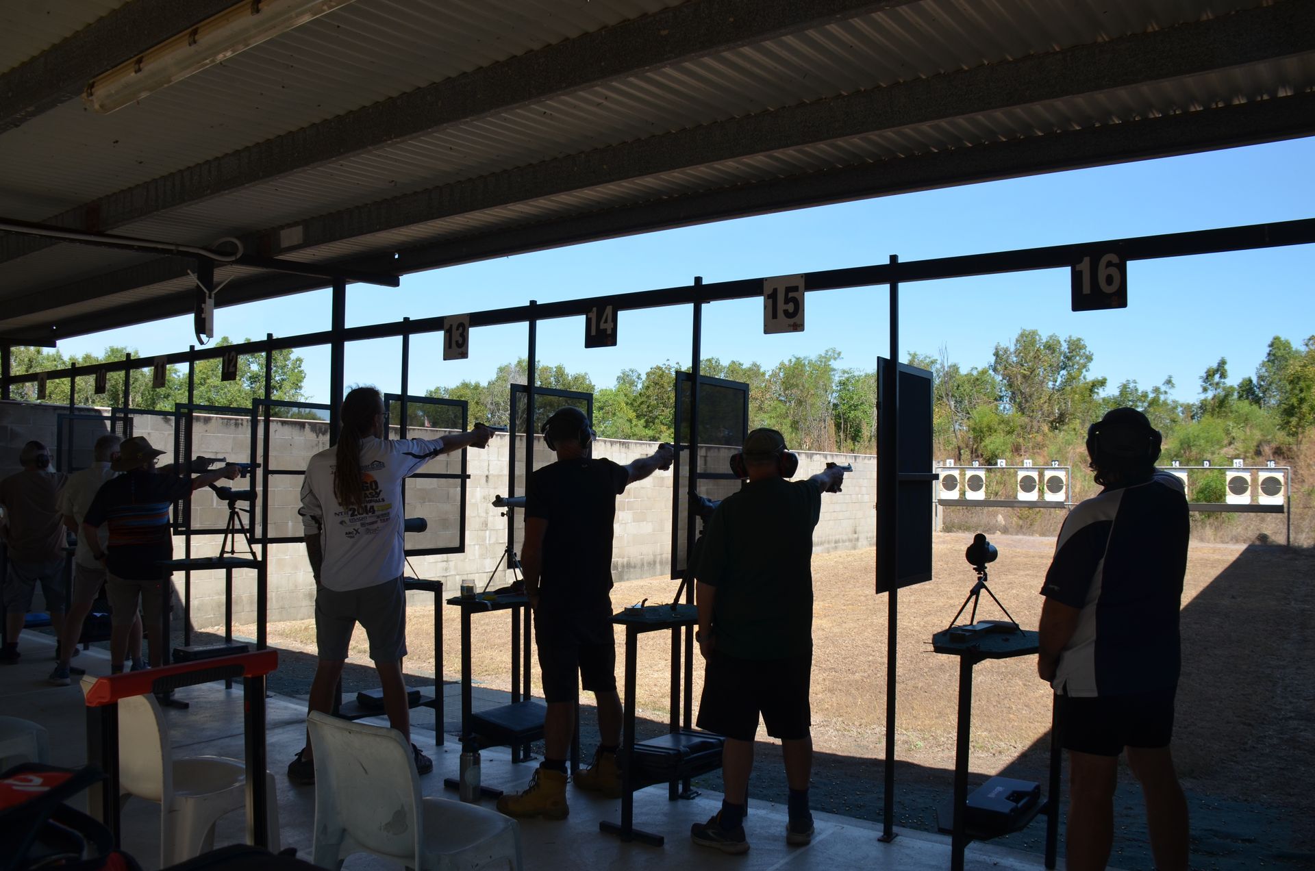 People shooting at targets on a sunny day at an outdoor gun range.