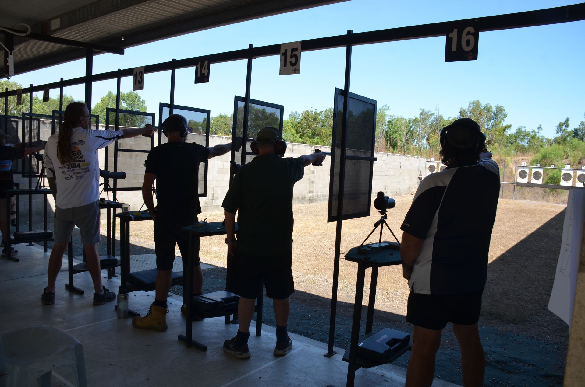 People shooting handguns at a firing range on a sunny day.