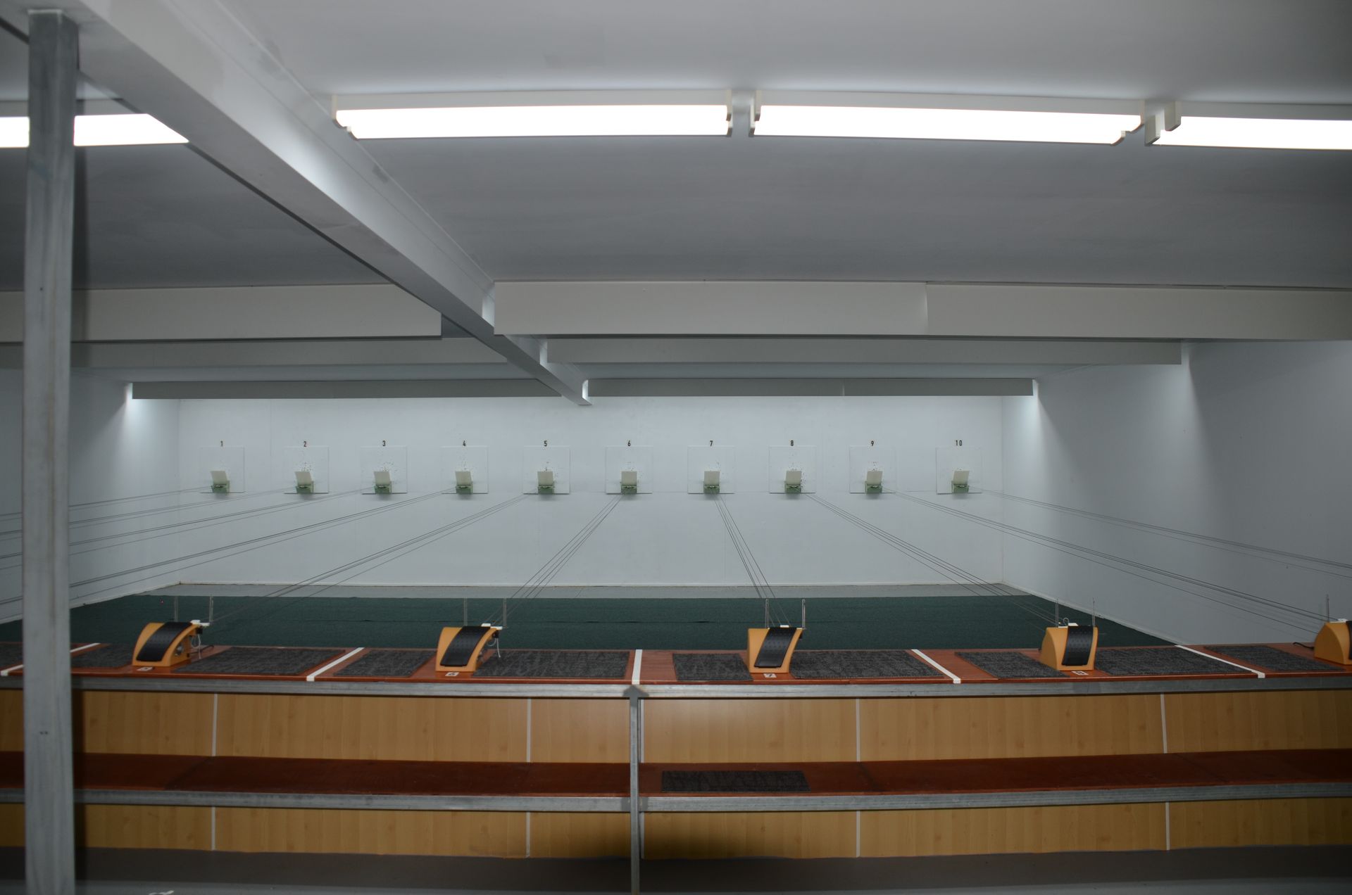 Shooting range interior: brown and orange shooting stations face targets downrange under white ceiling lights.
