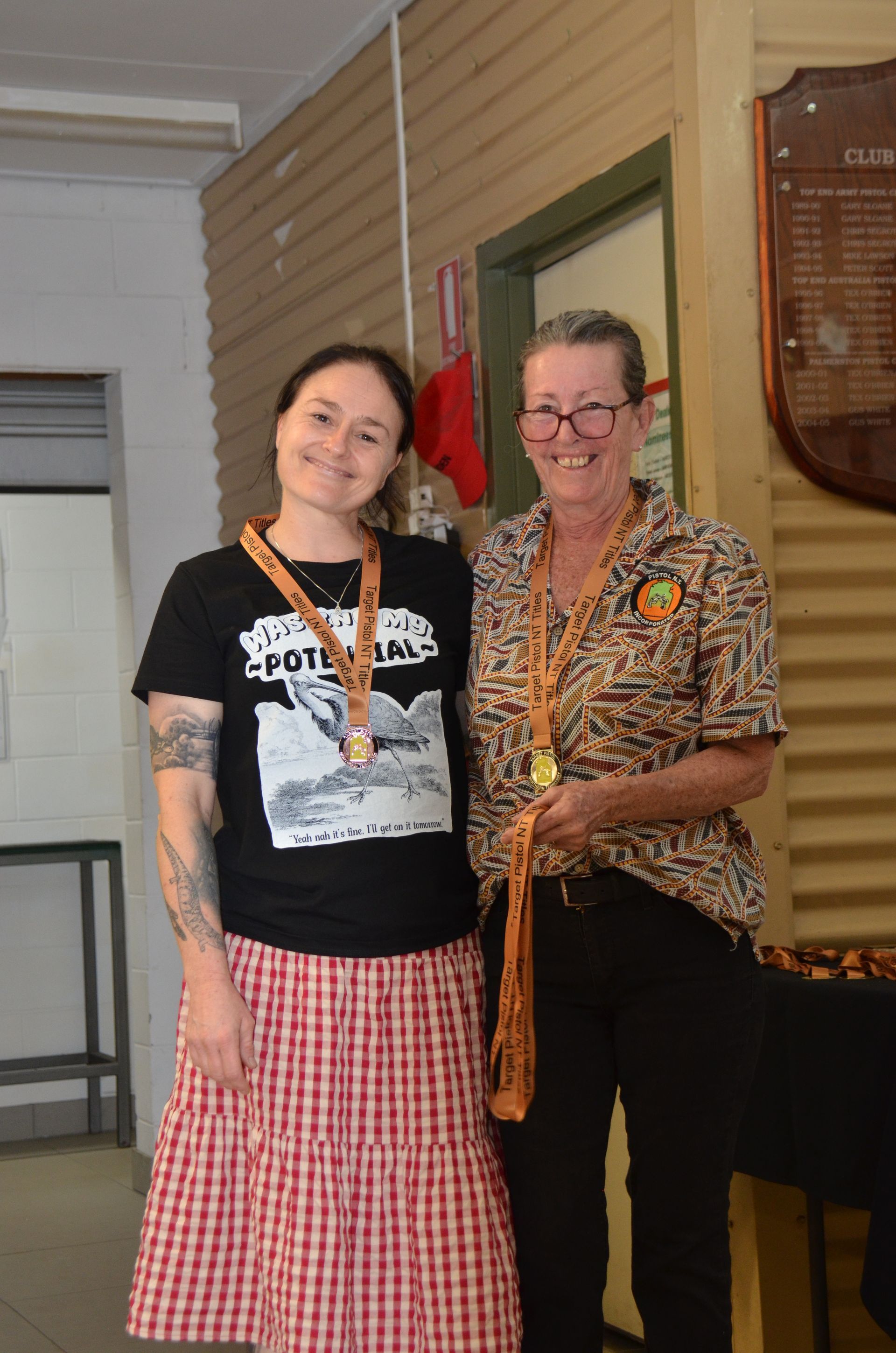 Two women smiling, wearing medals, standing inside a building. 