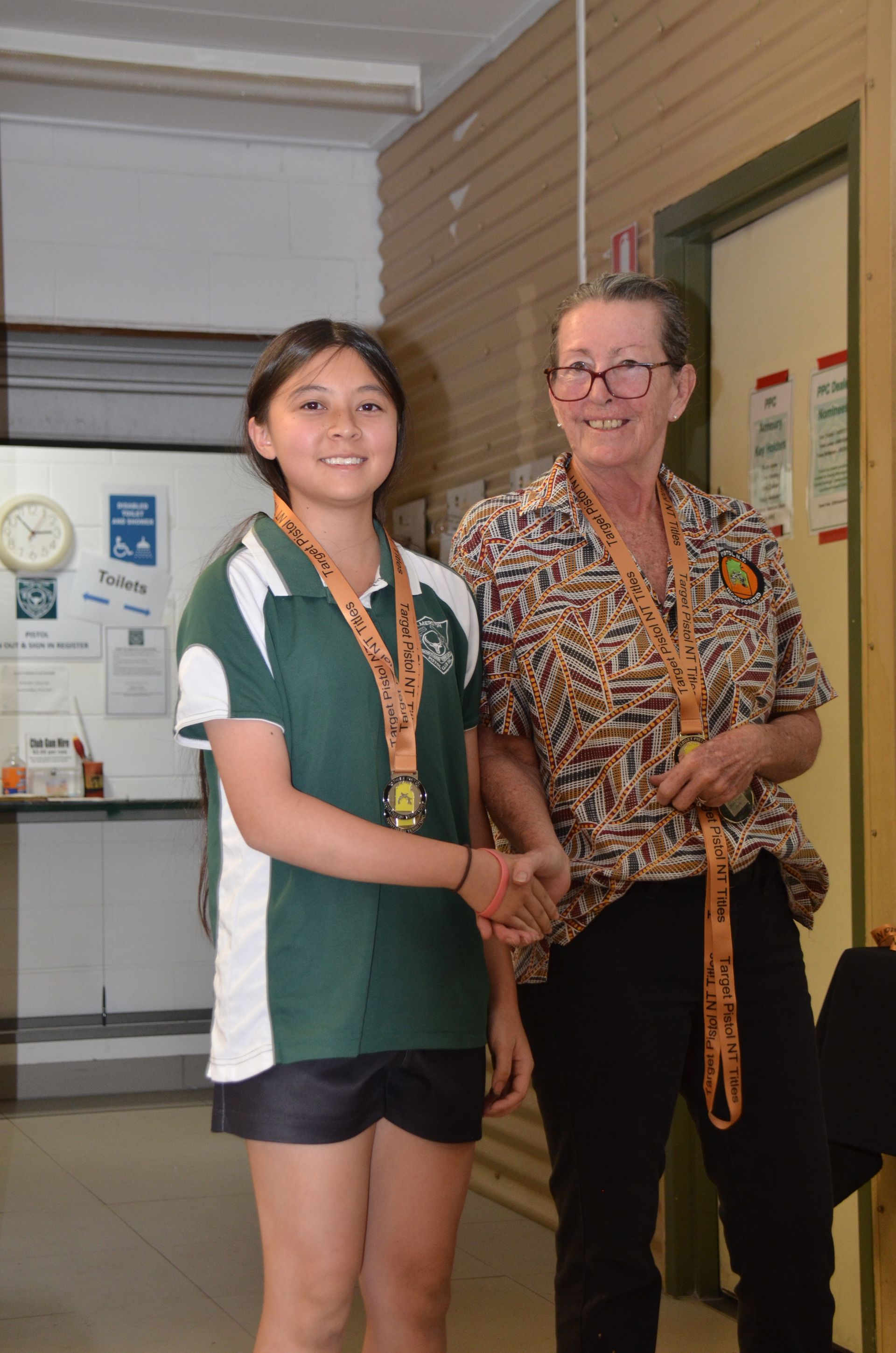 A young girl shakes hands with an older woman, both wearing medals.