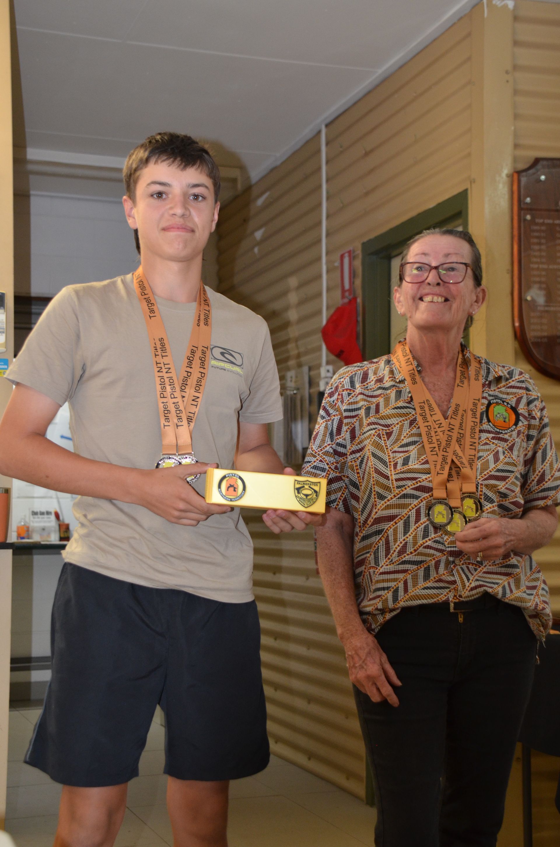 Teenager and woman holding awards, wearing medals, smiling, indoors.