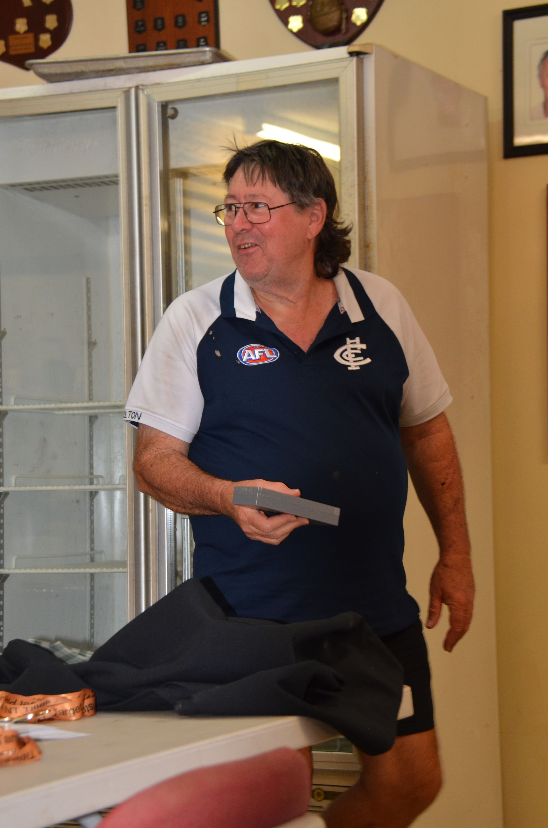 Man in blue collared shirt, shorts, standing near fridge. Holding object, looking right.