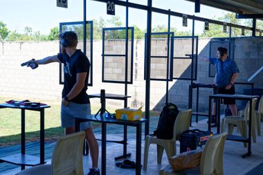 Two people firing handguns at an outdoor shooting range.
