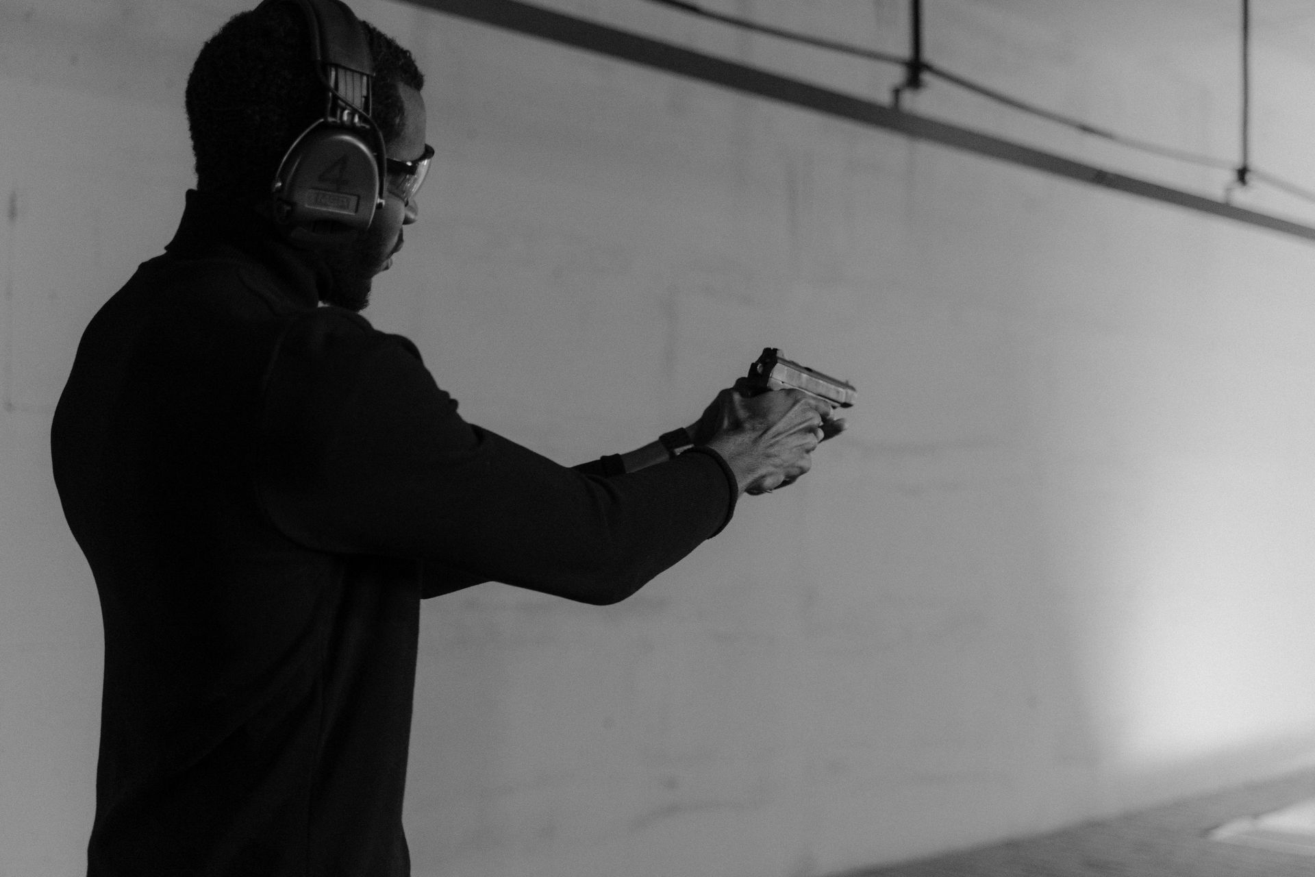 Man at shooting range, holding a pistol, wearing ear protection.