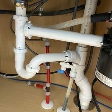 A sink with a lot of pipes and wires underneath it.
