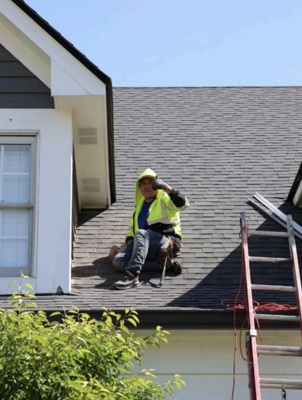 A man is sitting on the roof of a house next to a ladder.