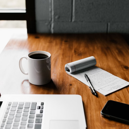 A cup of coffee sits on a desk next to a laptop