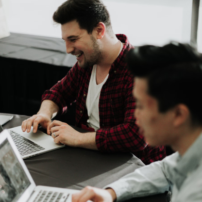 Two men are sitting at a table using laptops