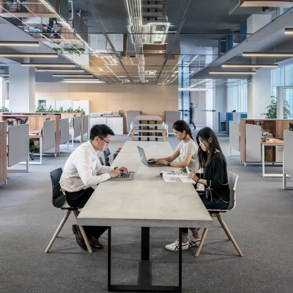 A group of people are sitting at a long table using laptops