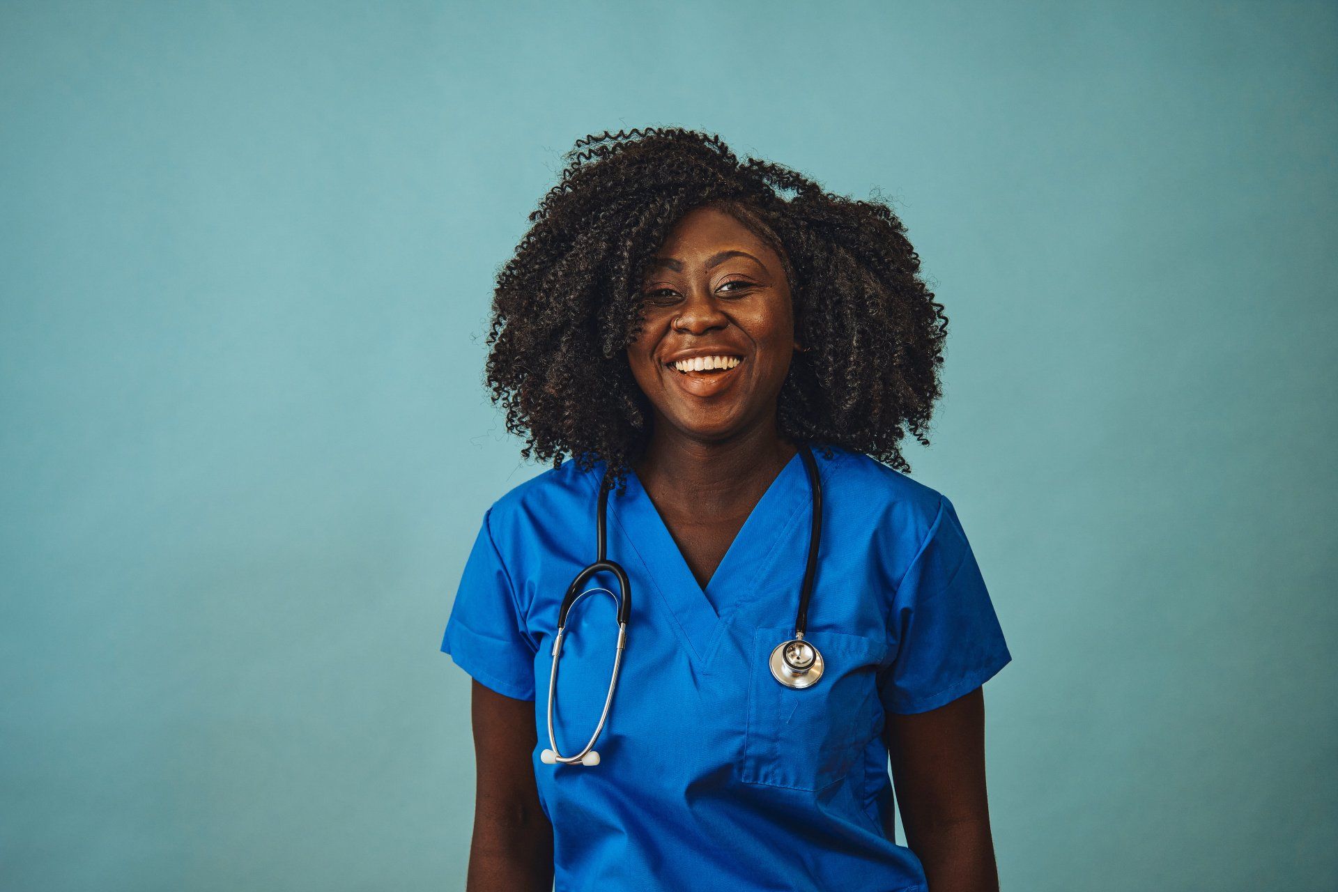 a woman in a blue scrub with a stethoscope around her neck is smiling